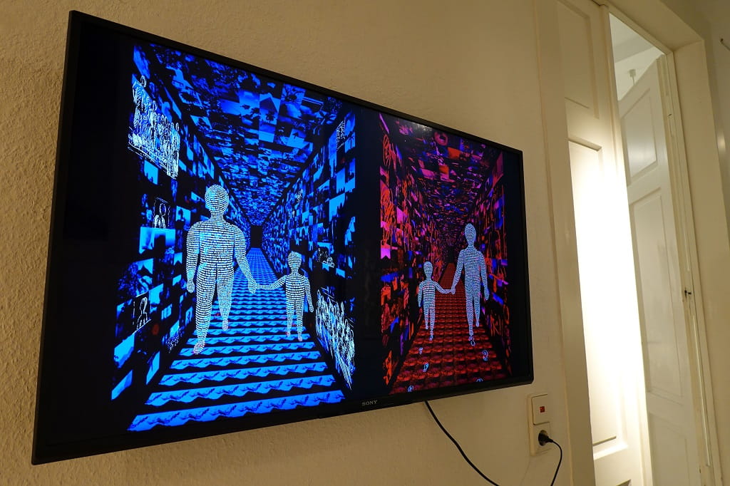 An der Wand montierter Bildschirm zeigt zwei nebeneinander angeordnete, farblich kontrastierende Tunnelräume aus vielen Bildern; darin gehen stilisierte Figuren Hand in Hand.